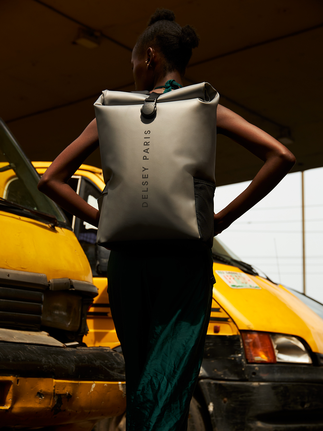 Staande vrouw voor auto's met een Delsey Turenne Soft rolltop rugzak op haar rug. 